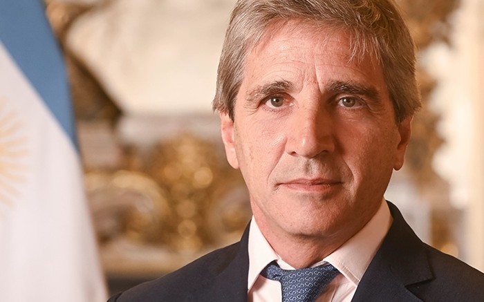 Luis Caputo, ministro de Economía, de traje oscuro y corbata azul, con la bandera argentina detrás