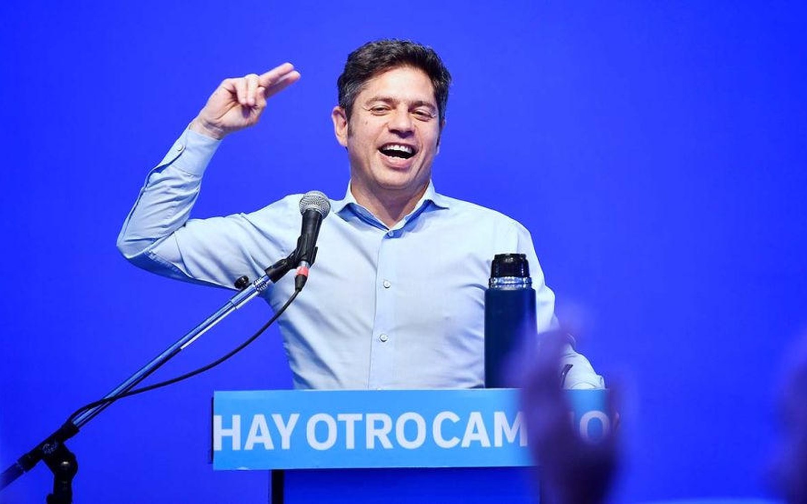 Axel Kicillof habla en un acto, de camisa celeste, con el puño levantado