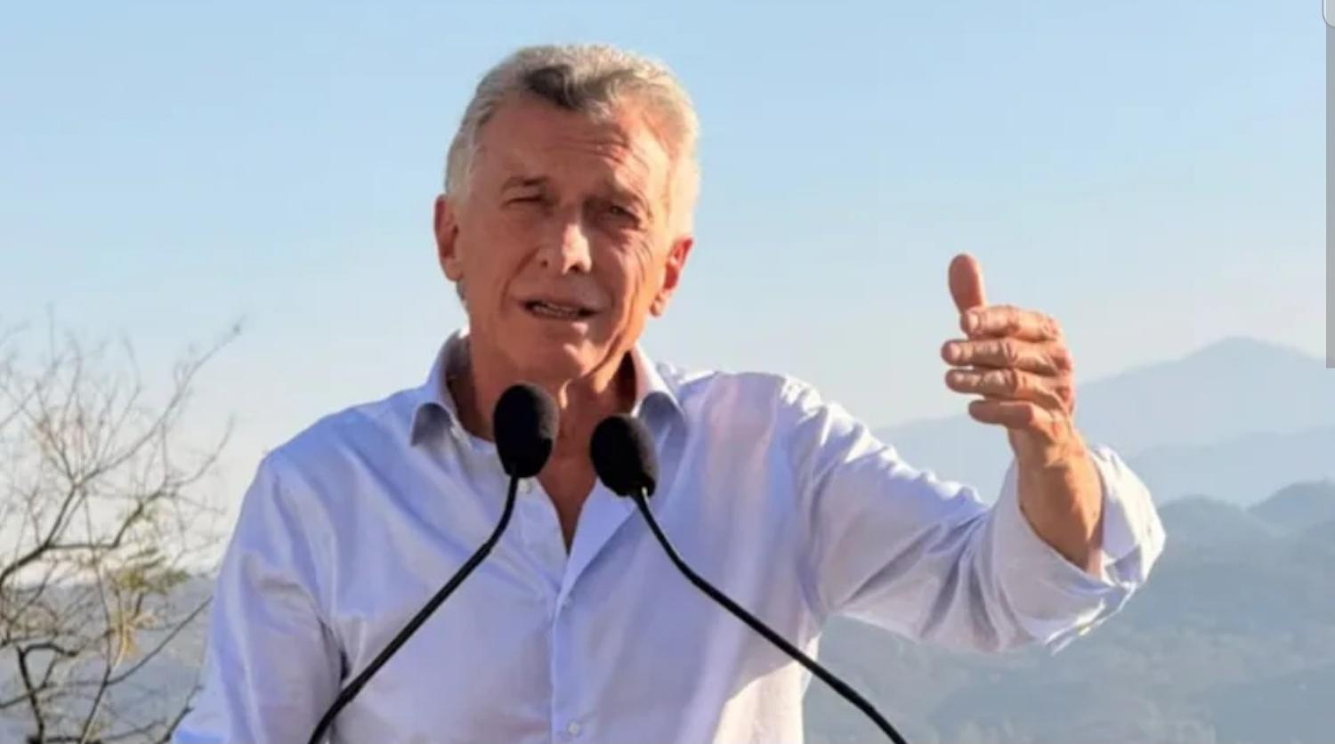 Mauricio Macri hablando en un acto, con dos micrófonos, y el pulgar levantado, con las montañas atrás