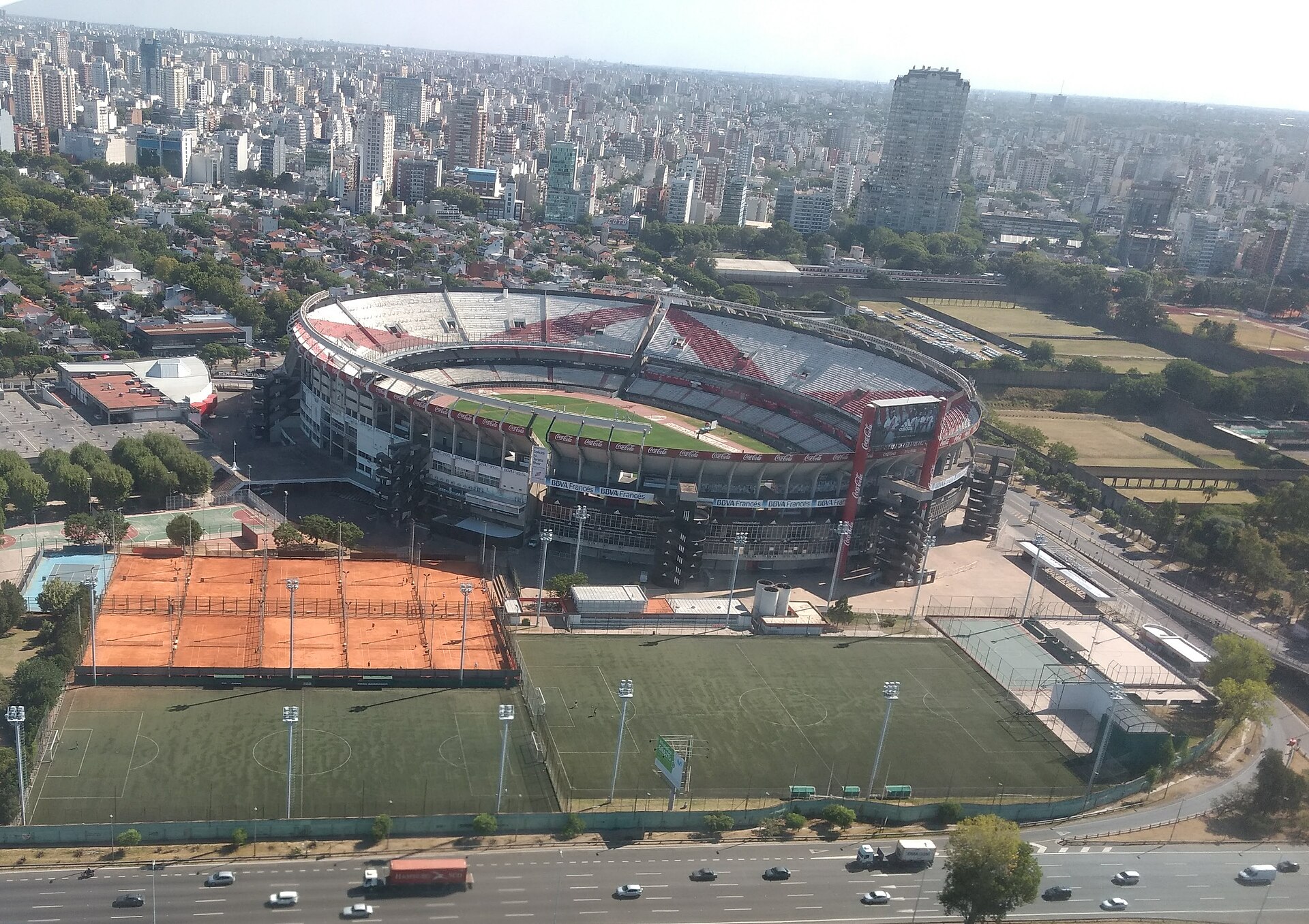Vista aérea del estadio Monumental de River Plate en Núñez, con el óvalo, la bandera roja y blanca y la ciudad detrás