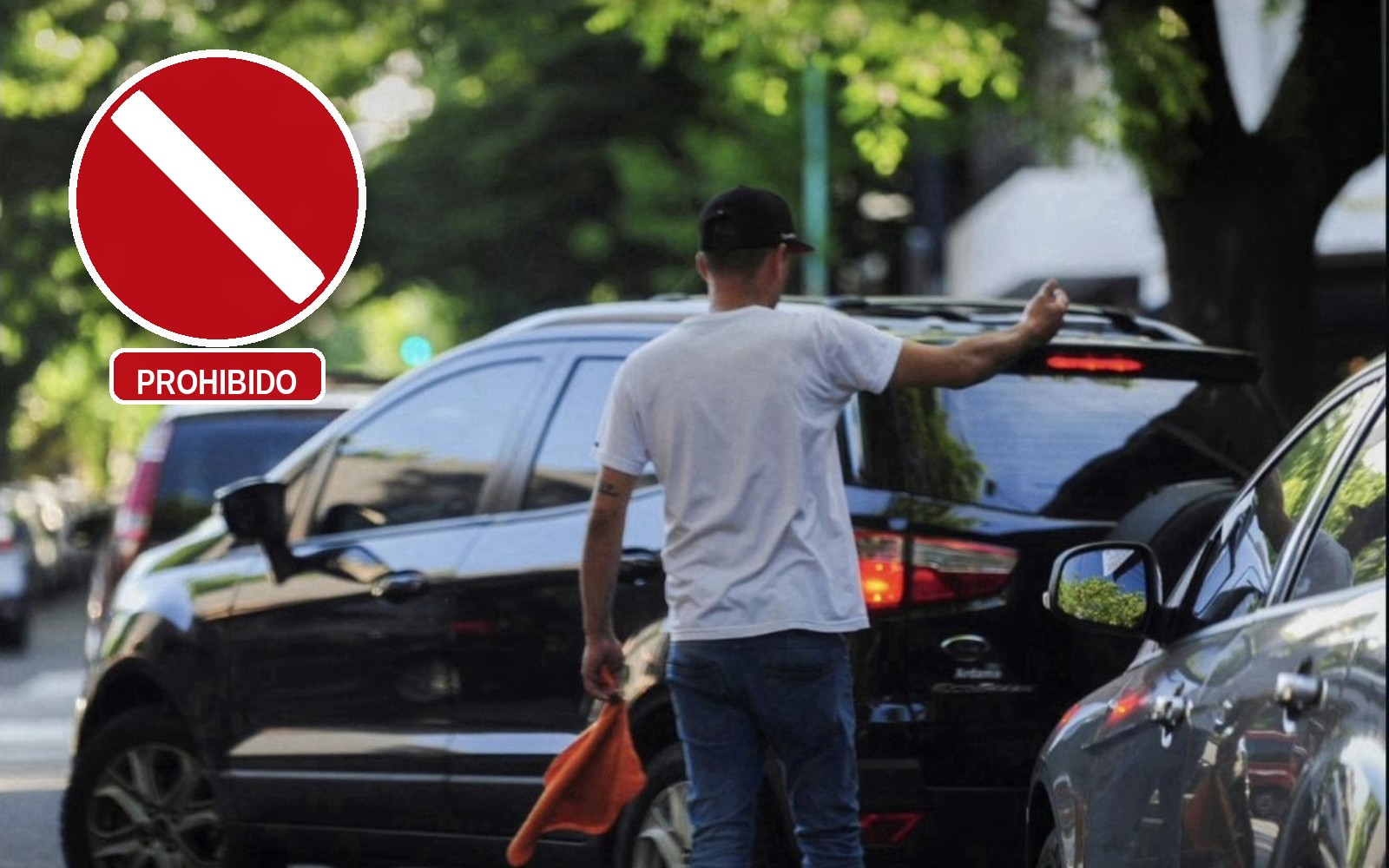 Un trapito de espaldas, con gorra negra y un trapo naranja, señalándole el lugar a un auto