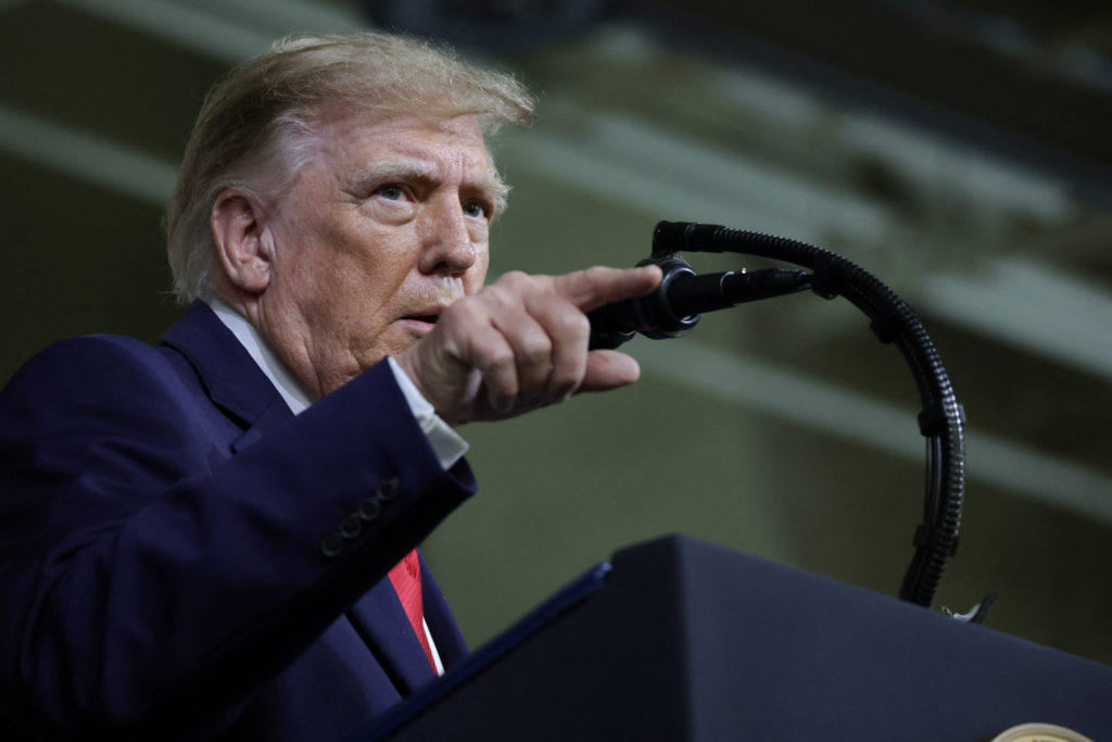 Donald Trump, de traje azul y corbata roja, hablando en un atril y señalando hacia adelante
