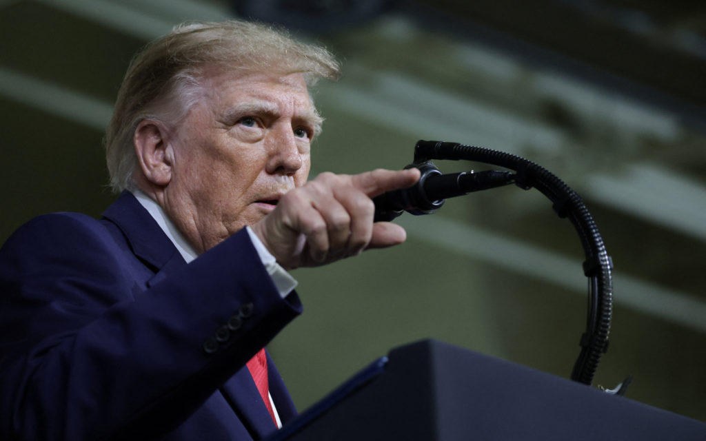 Donald Trump, de traje azul y corbata roja, hablando en un atril y señalando hacia adelante